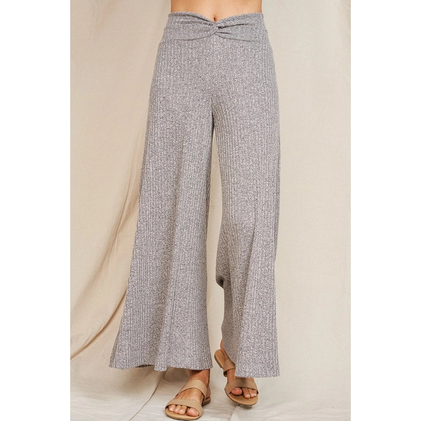 Another front view of a pair of rib knit soft comfy heather grey drapey wide leg flare pants with a waistband that is twisted in the front center. Model has leg raised to show the drapey, flowy movement of the material.